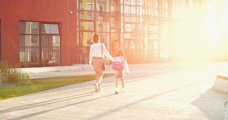 Rear of Caucasian beautiful mother and cute daughter in masks going to lessons outdoors in sun...