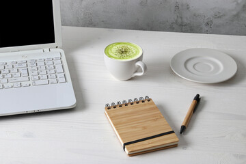 Office table with laptop, notebook and a cup of macha latte - obrazy, fototapety, plakaty