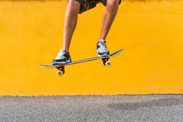 View of man legs jumping with skateboard on yellow background.