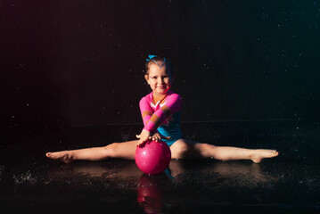 a cute little girl gymnast in a pink blue swimsuit does stunts underwater in an aqua studio on a...
