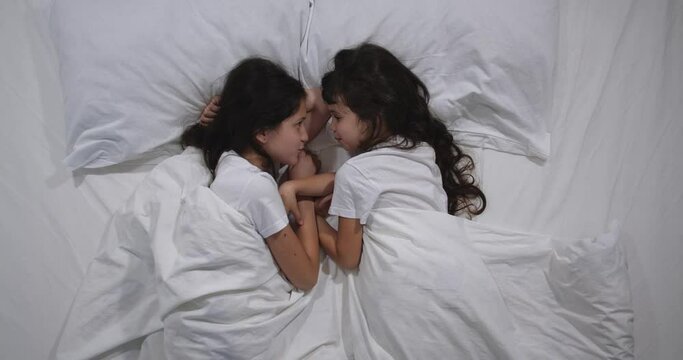 Top view of Caucasian  two children quarreling in bed with white sheets. High angle shooting. Little sisters argue, take offense at each other then they make up on their little fingers and smile.