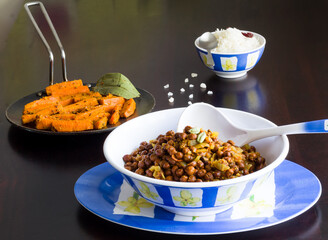 Bengal gram or kala chana masala,black chickpea gravy is gravy made of lentils during Navratri,Janamashtami celebrations in India.Served with sauteed carrots,steamed rice. Front view,dark background.