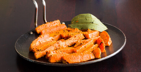 Sauteed Carrots,cooked in butter and Indian spices like bay leaf,paprika,fennel. Front view, closeup of diced,healthy,homemade carrot vegetable in cast iron pan. Isolated on dark wooden background