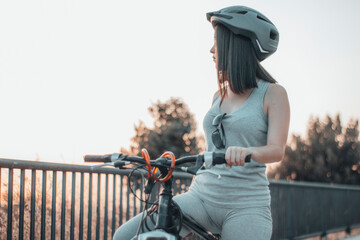 Muchacha joven parada y aparcada con una bicicleta y casco en la ciudad junto a los arboles y la...