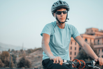 Hombre joven serio con casco haciendo ejercicio con la bicicleta en la ciudad junto a un parque