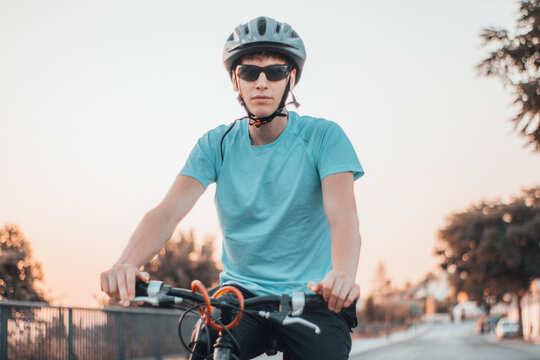 Hombre joven serio con casco haciendo ejercicio con la bicicleta en la ciudad junto a un parque