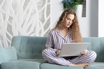 Portrait of  woman working on notebook at home in cozy atmosphere. Adorable girl sitting with laptop on couch in pyjamas. Businesswoman job and morning concept