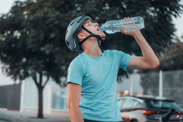 Chaval joven bebiendo agua después de hacer deporte con la bicicleta en la ciudad