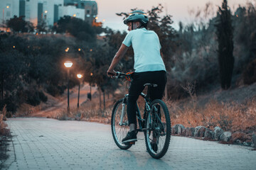 Hombre joven paseando con una bicicleta de espaldas con un casco de protección en un parque al...