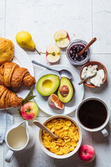 Breakfast table with cornflakes, croissants, fruit, cheese and cup of coffee. Gray tile background, top view.