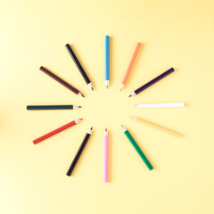 Creative layout made of colorful crayons. School concept with copy space on pastel yellow background.