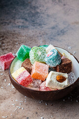 Turkish delight of different types in coconut bowl, dark background.