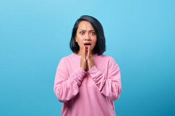 Shocked Asian woman covering mouth with palm isolated on blue background