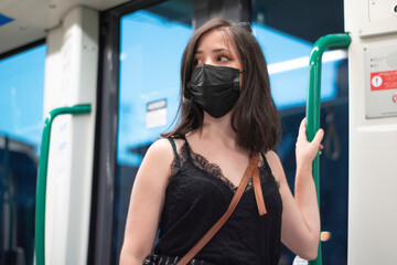Chica joven de pelo oscuro con mascarilla de pie en el interior del tranvía sujetando los barrotes