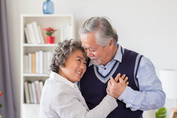 Fototapeta premium Happy Asian senior man embracing his wife on Christmas day at home. Senior couple spending time together with Christmas tree. Merry Christmas and Happy Holidays. Christmas holiday celebration