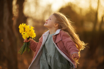 a little girl with yellow daffodils walks in the park