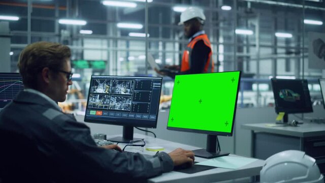 African American Engineer Using Laptop Computer and Looking Out of the Office at a Car Assembly Plant. Vehicle Factory Line Operator Working at Desk with Computer with Green Screen Display.