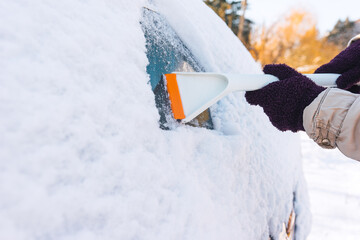 Woman in winter gloves cleans snow from car windows after snowfall