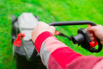 Lawn mower on green grass with sun light on the garden. Man holding mower dressed in red shirt....