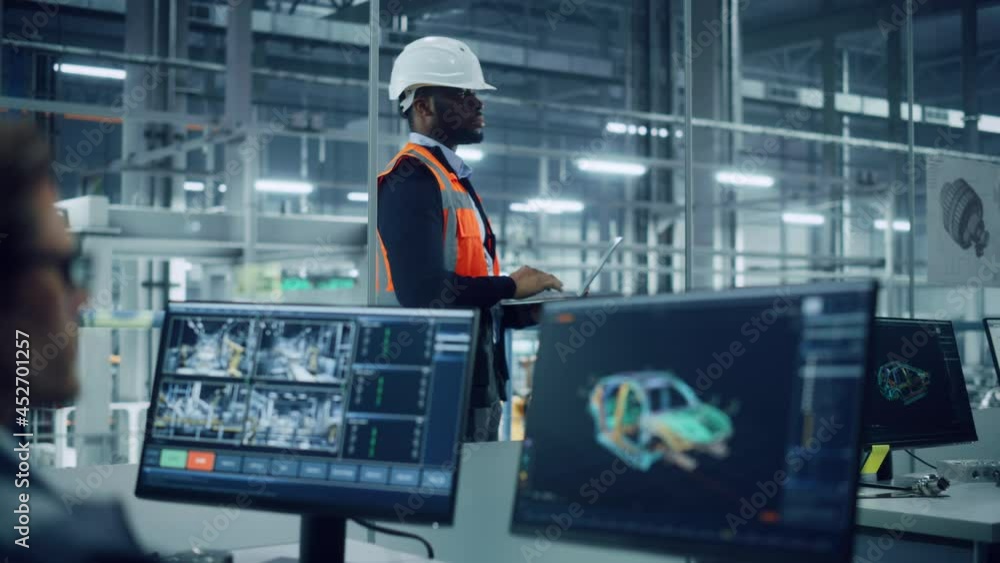 Poster African American Engineer Using Laptop Computer and Looking Out of the Office at a Car Assembly Plant. Vehicle Factory Line Operator Working at Desk, Overviewing Autonomous Electric Car Production.