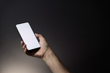 Man's hand holding black smartphone with blank white screen isolated on dark background