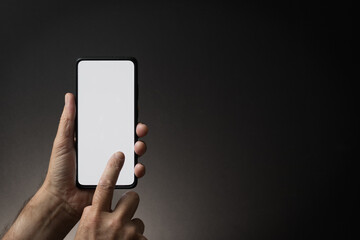 Man's hand holding black smartphone with blank white screen isolated on dark background