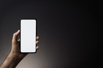 Man's hand holding black smartphone with blank white screen isolated on dark background