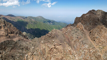 Stone peaks with cliffs. Grass grows in places. There is white snow on the glacier. There are signs made of stones and tablets. A mountainous area with large stones. Bogdanovich Glacier, Kazakhstan