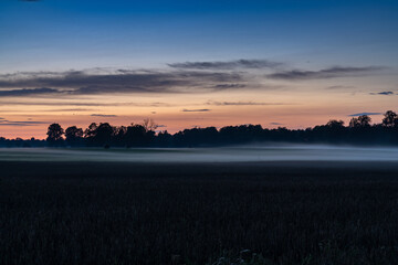 sunset and nightfall over farm fields and forest with a low fog creeping in