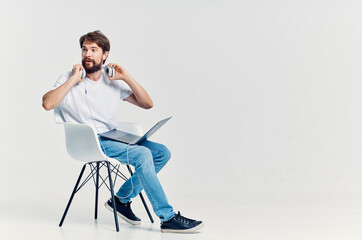 man in white t-shirt sitting on a chair with a laptop in headphones