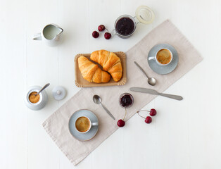 Naklejka na ściany i meble Tasty healthy food, breakfast, brunch or just snacks. Freshly baked croissants with jam from latest cherry harvest and fresh espresso. White wooden table background.