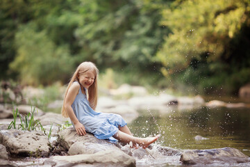 a little girl in a blue sundress with a bouquet of daisies walks by the river splashes of water