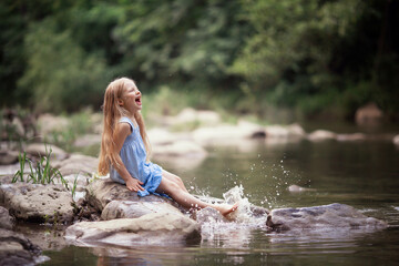 a little girl in a blue sundress with a bouquet of daisies walks by the river splashes of water