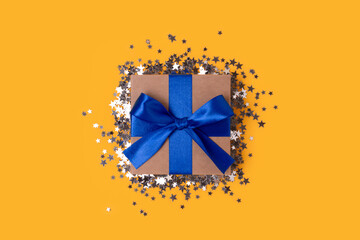 Gift box with blue ribbon and silver confetti on a yellow background.