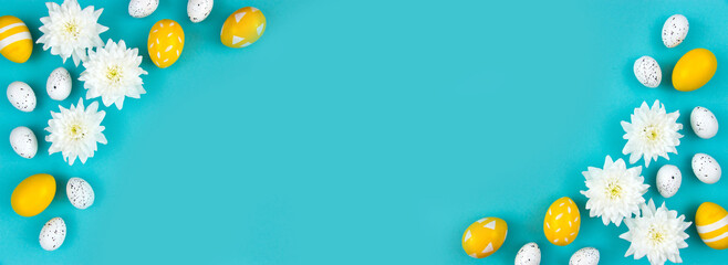 White flowers and painted Easter eggs on a blue background. Festive floral concept with clean text space. Flat lay. View from above.