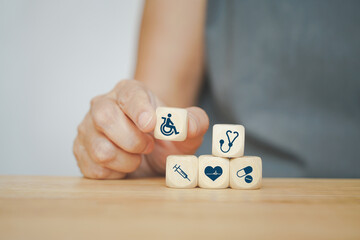 senior woman hand holding disability on wheelchair icon on wooden cube with medical icon on wood desk, annual health checking, health insurance, wellness, wellbeing concept