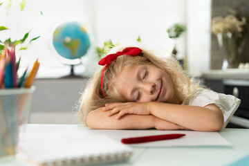 a little blonde girl is studying, tired of studying the child lay down on the table, the schoolgirl is tired