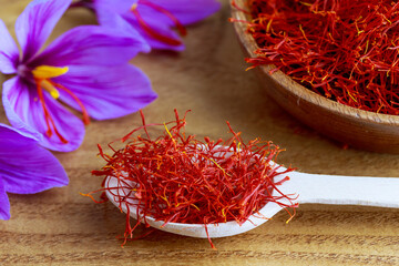 Saffron stamens in a wooden spoon. On the blossomed flower three red stamens which tear off and dry are visible.