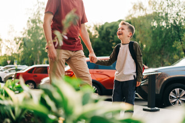 Happy father and kid son going to classes. Parent take child boy to school in first grade. Pupil of primary school go study with backpack outdoors in city street. Beginning of lessons. Back to school.