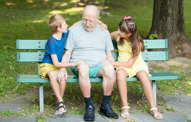 happy children and theri grandfather are playing time together on the bench in the park