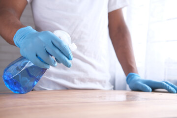 Fototapeta na wymiar hand in blue rubber gloves holding spray bottle cleaning table 