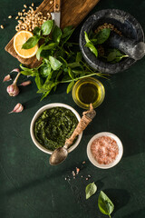  Pesto sauce in bowl with ingredients on rustic green table. Traditional Italian pesto recipe for making fettuccine, pasta, bruschetta.