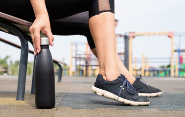 Happy woman working out on the sports ground in sunny summer day, drinking water from the bottle
