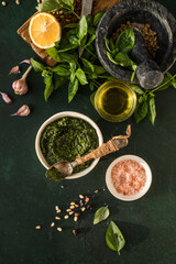  Pesto sauce in bowl with ingredients on rustic green table. Traditional Italian pesto recipe for making fettuccine, pasta, bruschetta.