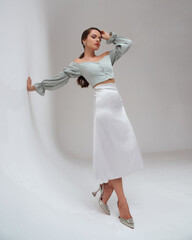 Elegant woman wearing pastel green top, silver silk skirt and high heels standing at white gray...