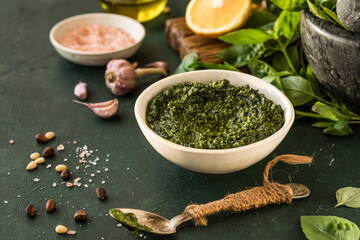  Pesto sauce in bowl with ingredients on rustic green table. Traditional Italian pesto recipe for making fettuccine, pasta, bruschetta.