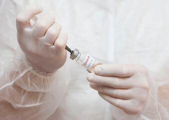 A man in a medical uniform holds an ampoule with a coronavirus vaccine in front of him and uses a syringe to collect the substance.