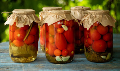 Pickled tomatoes in a glass jars on an old wooden table. Summer harvest.