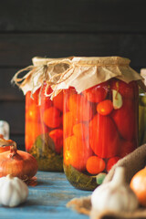 Pickled tomatoes in a glass jar on an old wooden table with a dark background