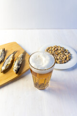 glass of lager beer with foam, Salty fish on cutting board and  pistaches on white background